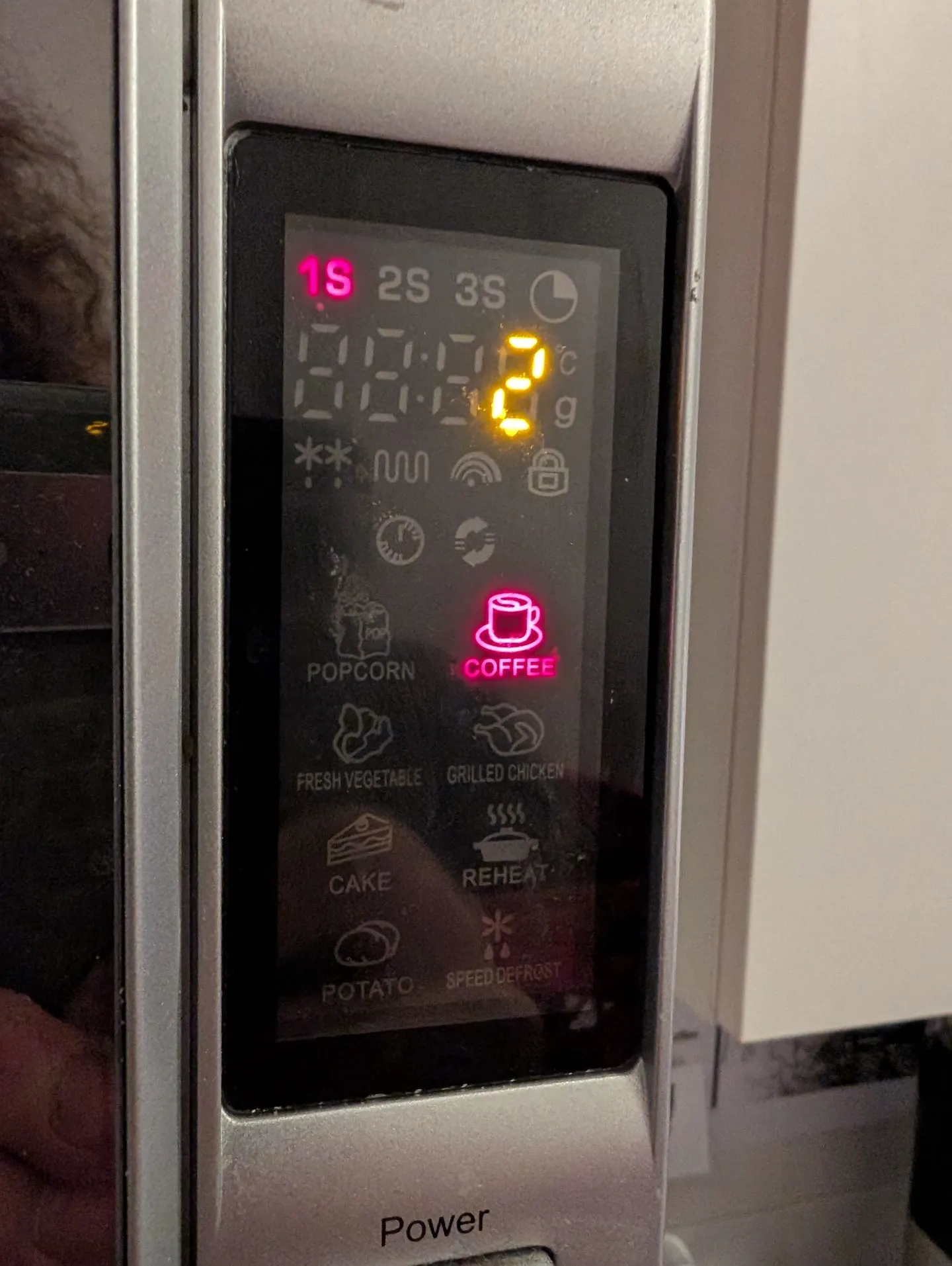 a microwave display, showing a red "coffee" icon, with "1S" illuminated in the top left, and an orange "2". it also shows a bit of my hair int he reflection