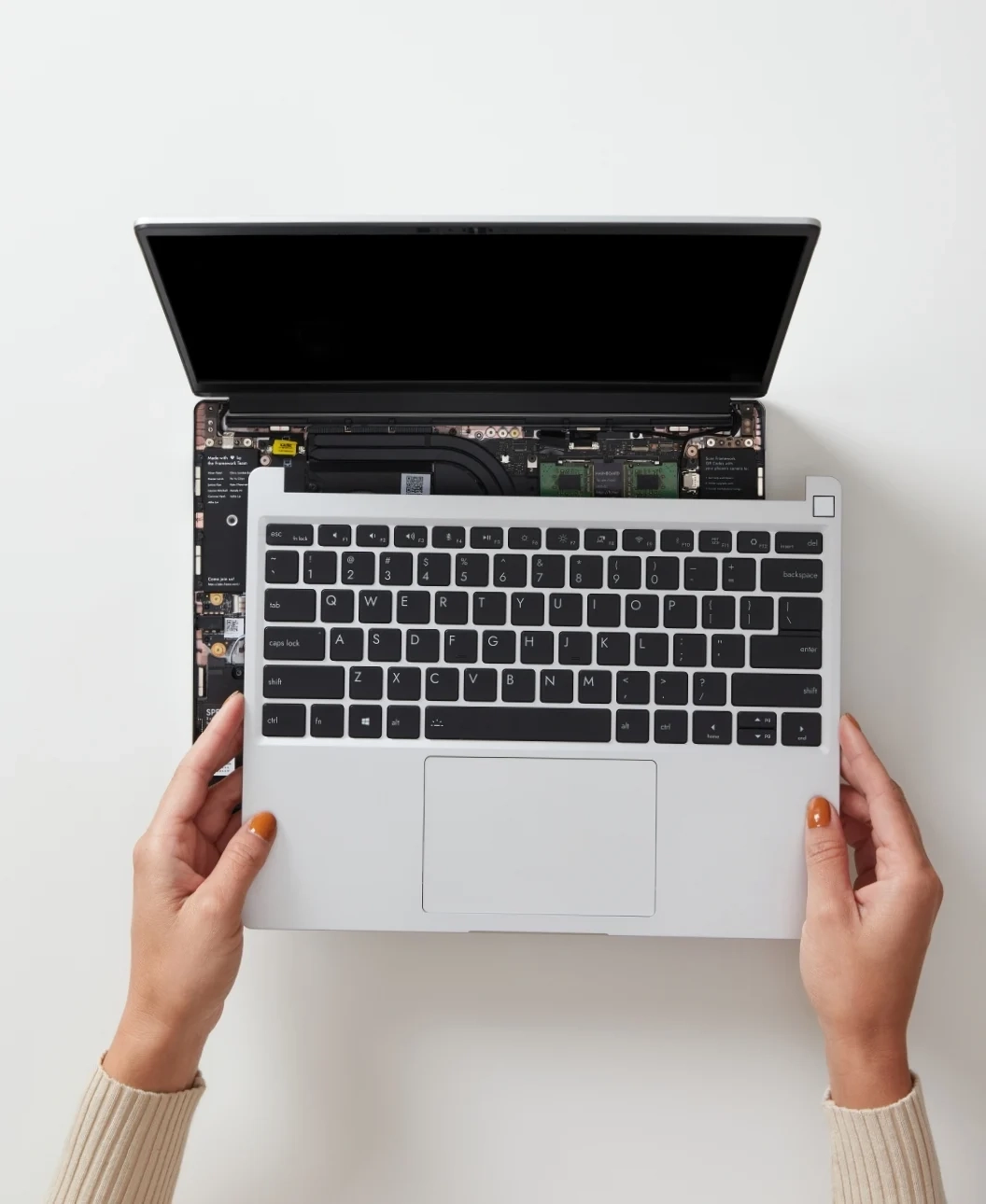 a top down picture of the framework laptop with someone holding the top cover with the keyboard. it is visible that the enter key and \| key share the same "pocket" as there's no aluminium in between the keys