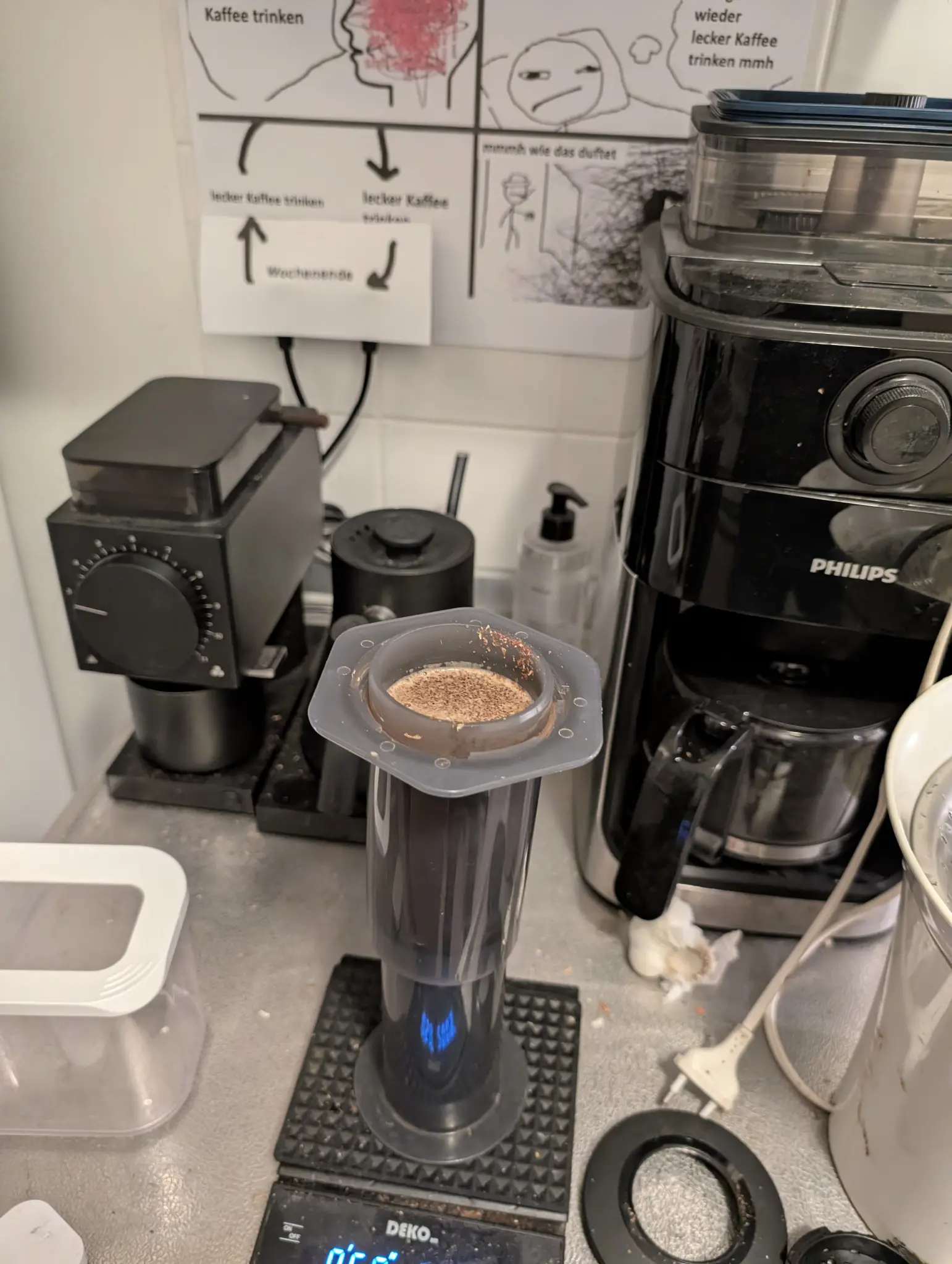 An aeropress (inverted) brewing some  coffee, with the "lecker kaffee trinken" "meme" in the background