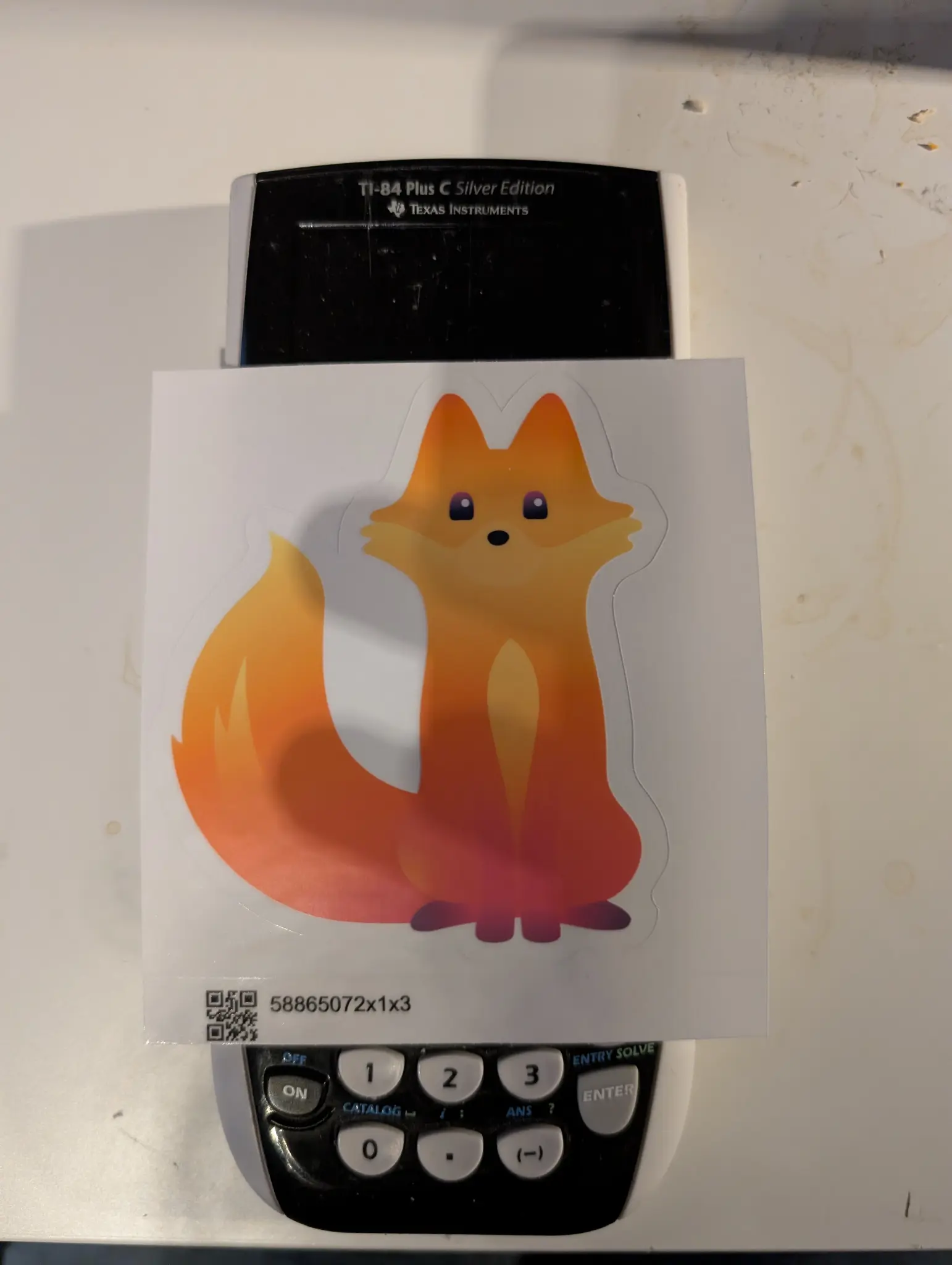 a sticker of kit, the cute firefox mascot, on top of a calculator, showing the sticker is roughly the same width