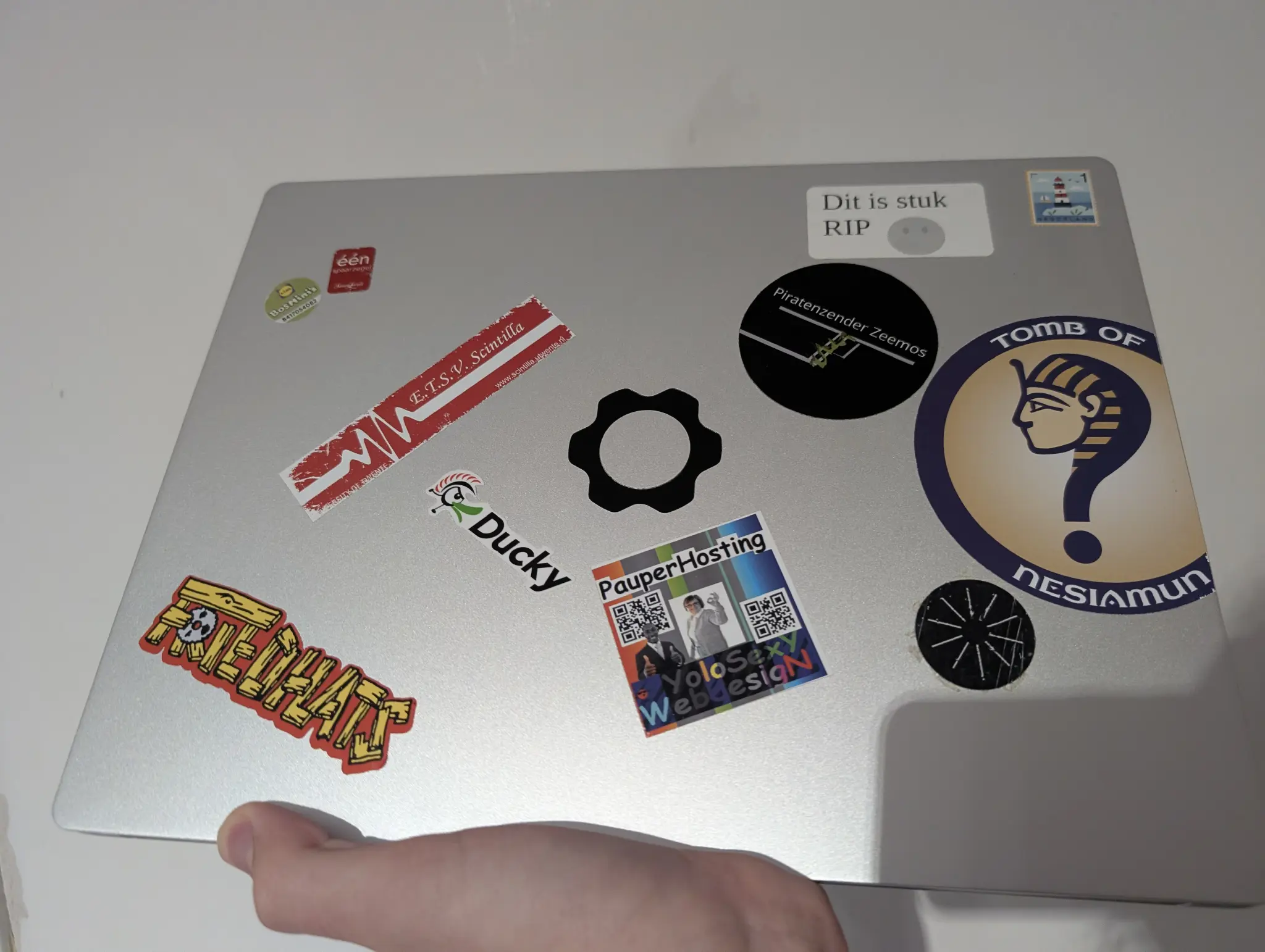 laptop with a couple stickers, lile PauperHosting, "Dit is stuk RIP", a postage stamp and a couple supermarket loyalty stamps